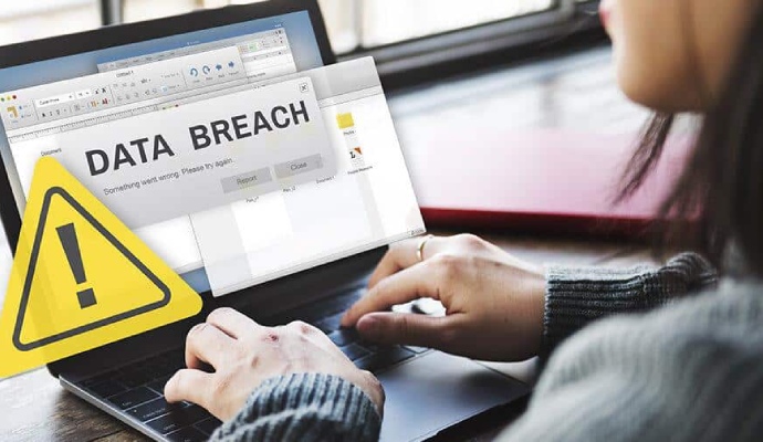 A person using a laptop with a prominent yellow warning icon and a 'DATA BREACH' alert message displayed on the screen.