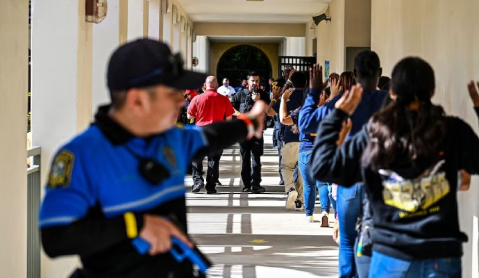 Students with hands raised walk through a school hallway during an active shooter drill