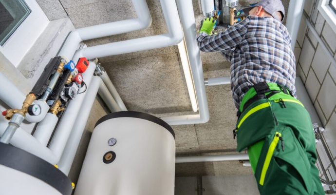A technician inspecting insulated white pipes and a large boiler tank