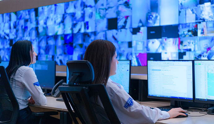 Security professionals monitoring a large-scale video wall and multiple computer screens in a high-tech surveillance operations center