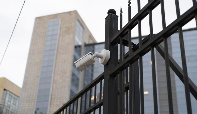 Security camera mounted on black metal fence with a modern office