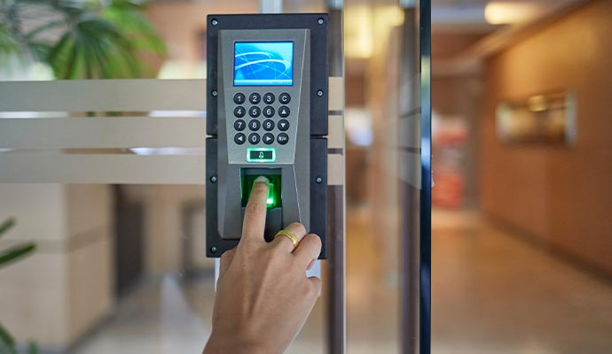 Person using a biometric fingerprint access system with keypad entry for secure building access