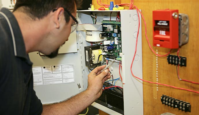 Technician performing maintenance on a fire alarm control system and electrical panel