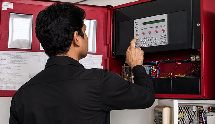Technician inspecting and testing a fire alarm control panel