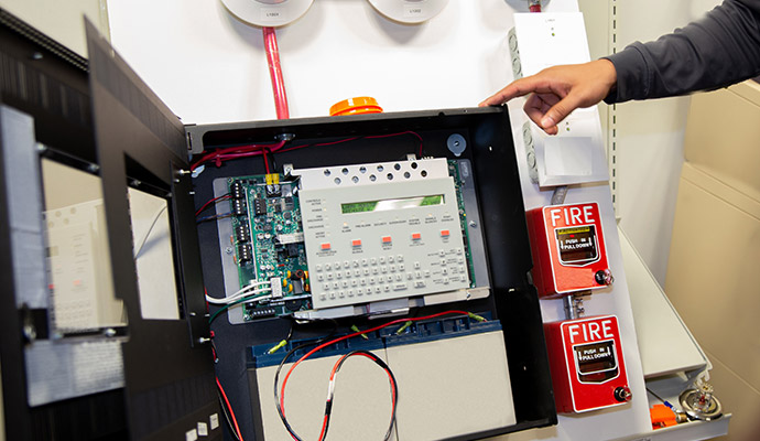 Technician pointing to open fire alarm panel and pull stations