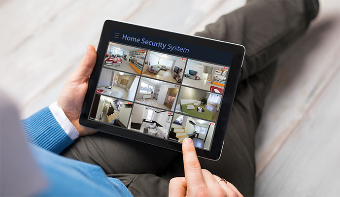 A person holding a tablet displaying live video feeds from multiple home security cameras to monitor different rooms of a house.