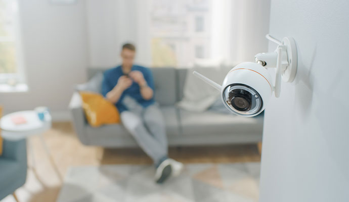 A white wireless IP security camera mounted on a wall, providing indoor video surveillance of a living room area.