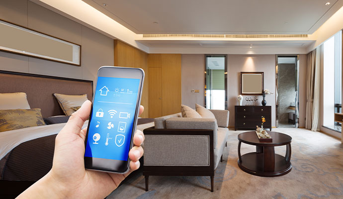Hand holding a smartphone displaying a smart home automation app interface in a modern luxury bedroom.