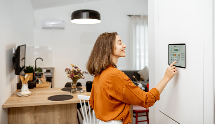 Woman adjusting smart thermostat and lighting on a wall-mounted control panel