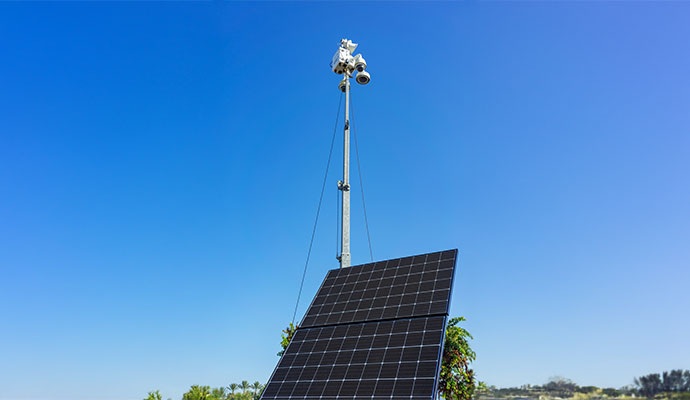 Tall security mast standing behind ground mounted solar panels
